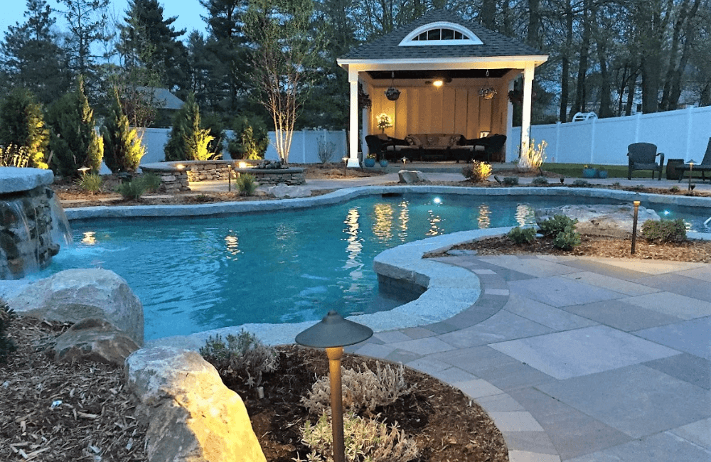 Dark backyard overlooking swimming pool with custom lighting